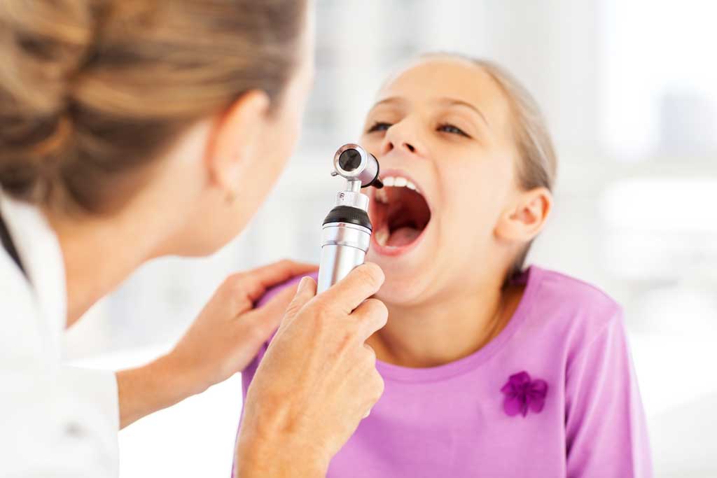 Female-doctor-examining-girl's-throat-with-otoscope-in-clinic-before-adenoidectomy