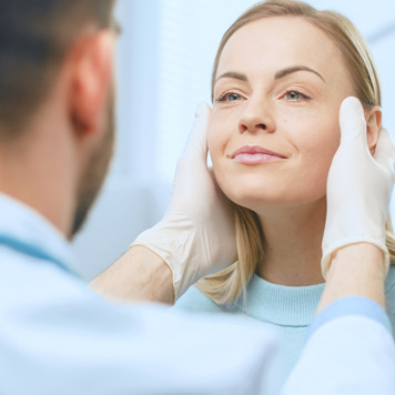 Male-plastic-surgeon-evaluating-female-patient’s-face Male-plastic-surgeon-evaluating-female-patient’s-face