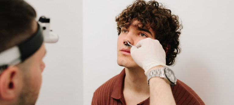 doctor-with-a-head-lamp-examining-a-young-man's-nose