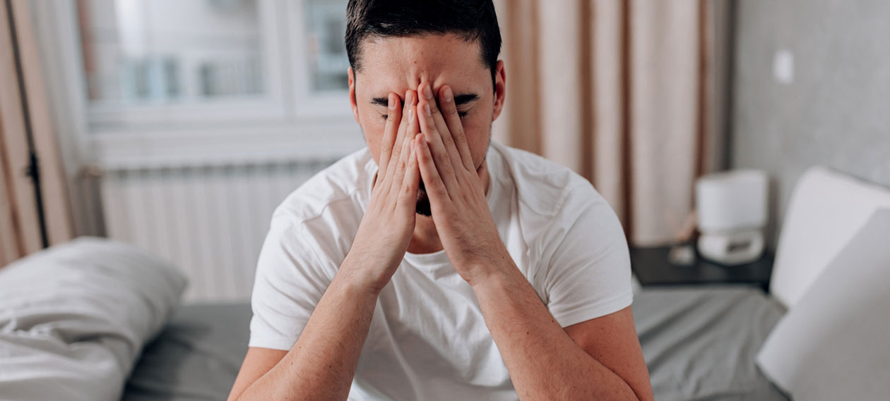 man-sitting-on-the-edge-of-a-bed-rubbing-his-face
